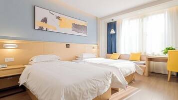 A hotel room with two beds, a desk, a chair, a window with curtains, and a painting on the wall.