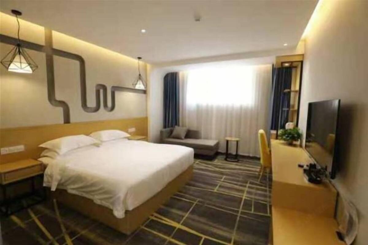 A hotel room with a large bed, a TV, a small seating area, and a desk.
