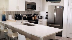 Une cuisine moderne avec des armoires blanches, des appareils en acier inoxydable et un grand îlot central doté de tabourets de bar.