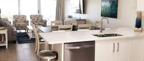 A modern kitchen with white cabinetry, a stainless steel dishwasher, and a dining area with a table and chairs.