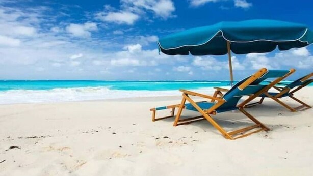 Une plage avec deux chaises longues en bois et un parasol bleu.