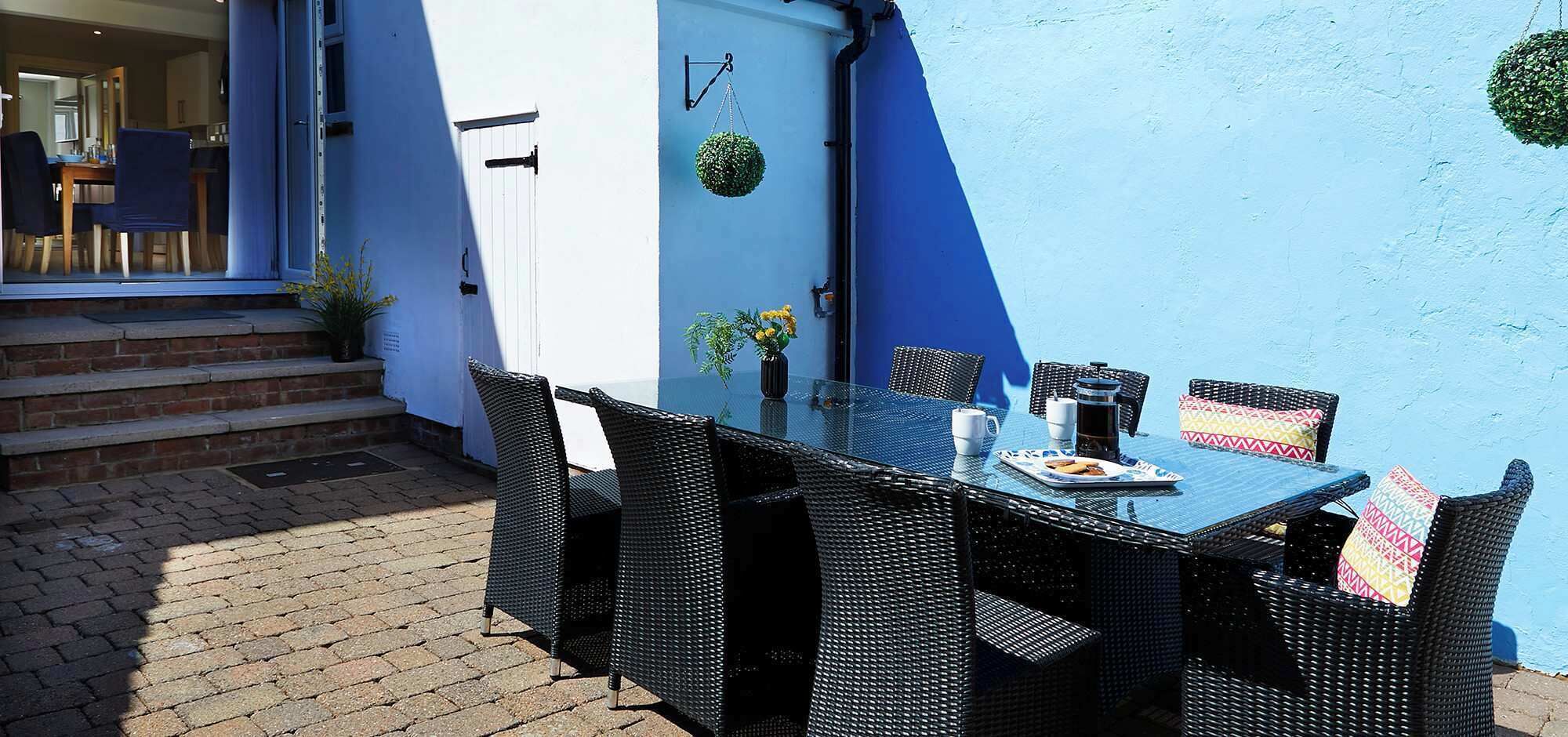 An outdoor dining area with a glass table and wicker chairs, a coffee maker, and a plate of food.
