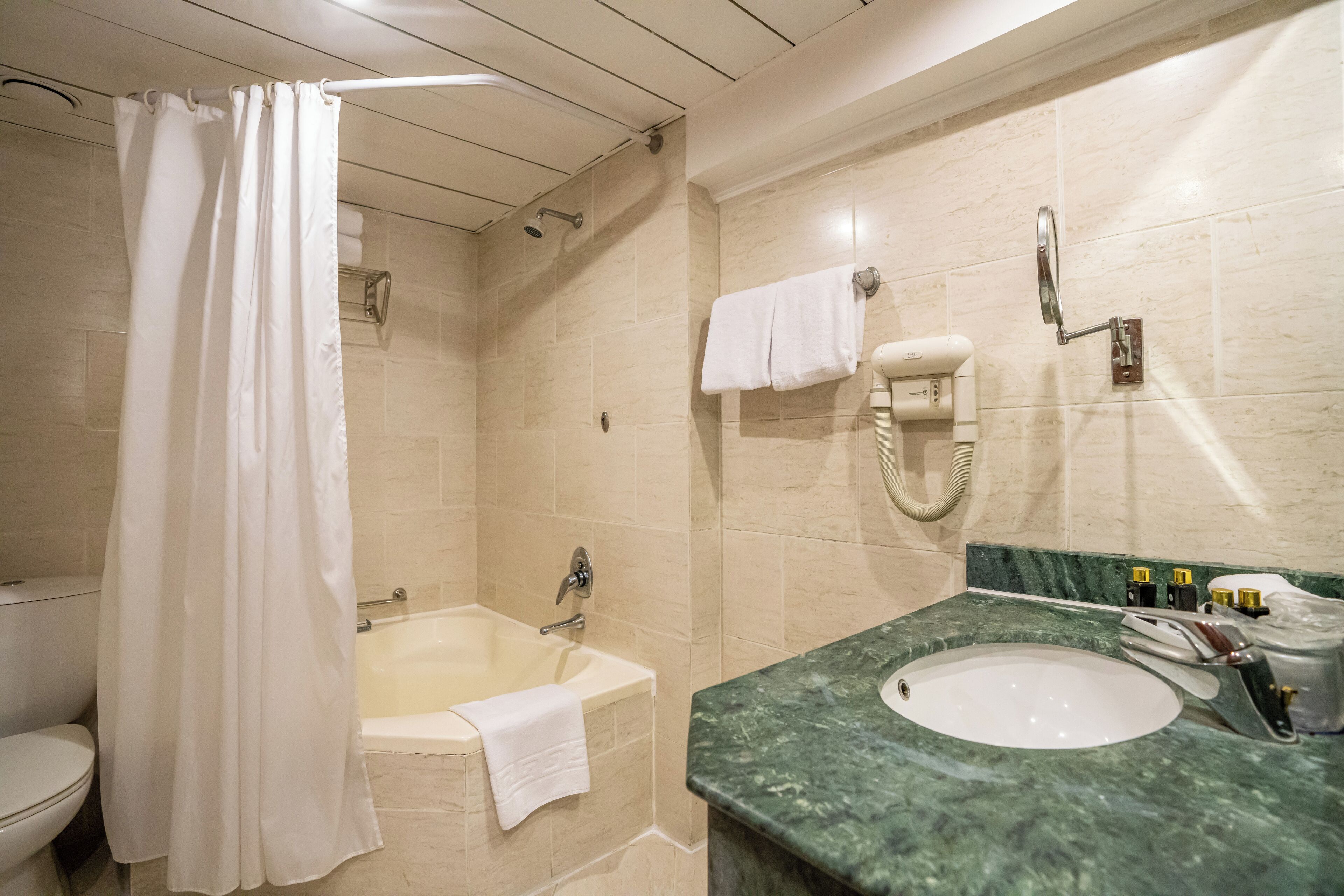 A bathroom with a bathtub, a shower curtain, a toilet, a sink, and a towel rack.