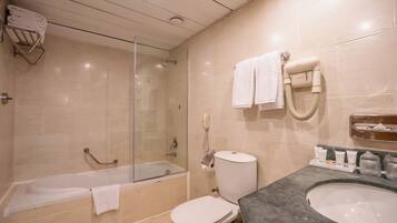 Un baño moderno con ducha envuelta en vidrio, una bañera, un inodoro y un lavabo con artículos de aseo.