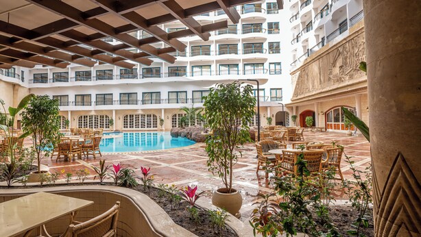 Un vestíbulo de hotel con piscina, zona de estar al aire libre y varios balcones.