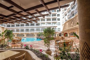 Un vestíbulo de hotel con piscina, mobiliario exterior y varios balcones.