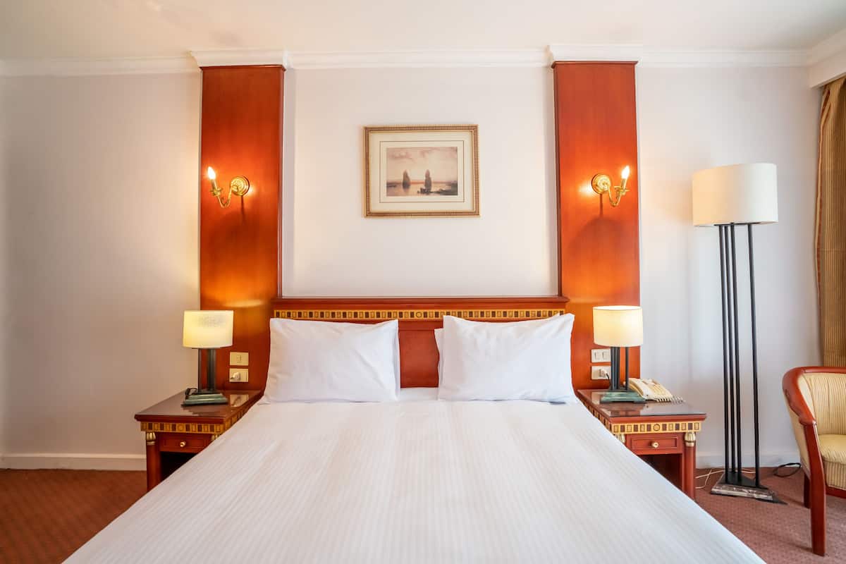 A hotel room with a large bed, two bedside tables with lamps, a framed picture on the wall, and a floor lamp.