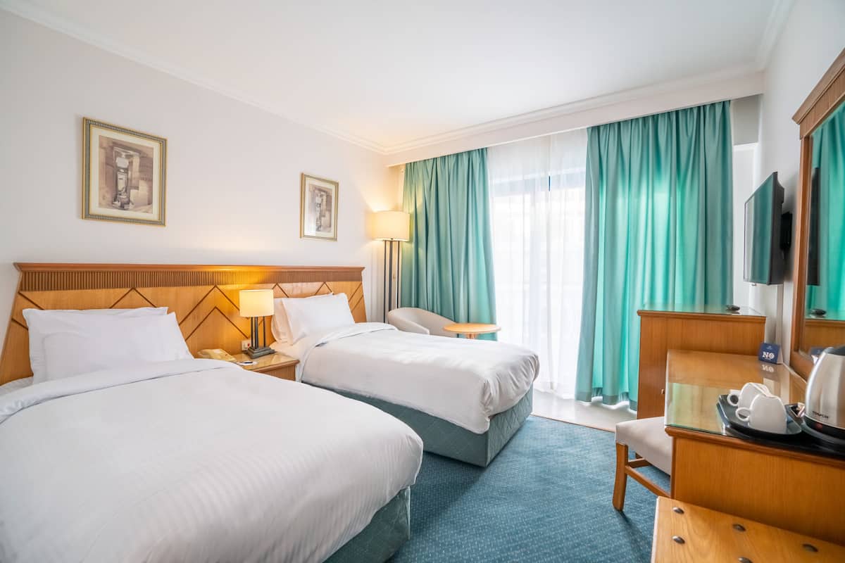 A hotel room with two beds, a desk, a chair, a TV, and a window with curtains.