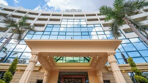 Un hotel moderno con fachada de vidrio, palmeras y una entrada clásica.
