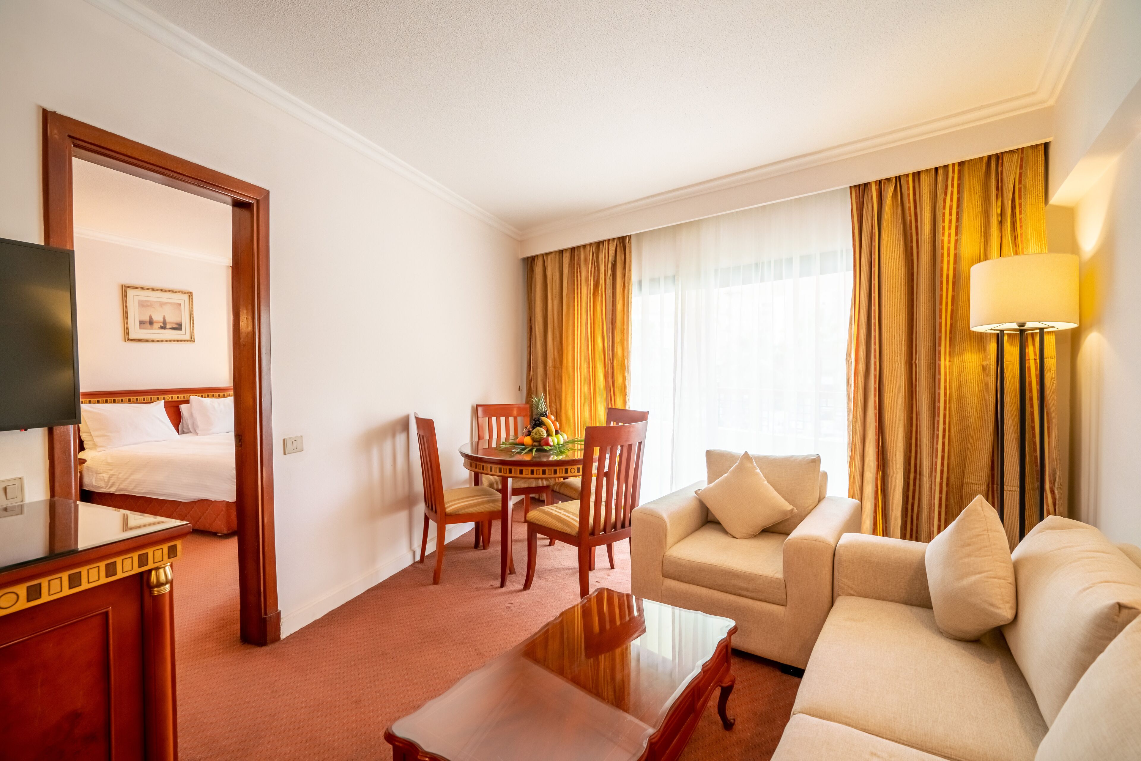 Una habitación de hotel con cama, sofá, mesa de comedor con sillas, televisor y lámpara.
