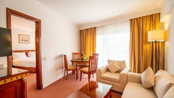 Una habitación de hotel con cama, sofá, mesa de comedor con sillas, televisor y lámpara.