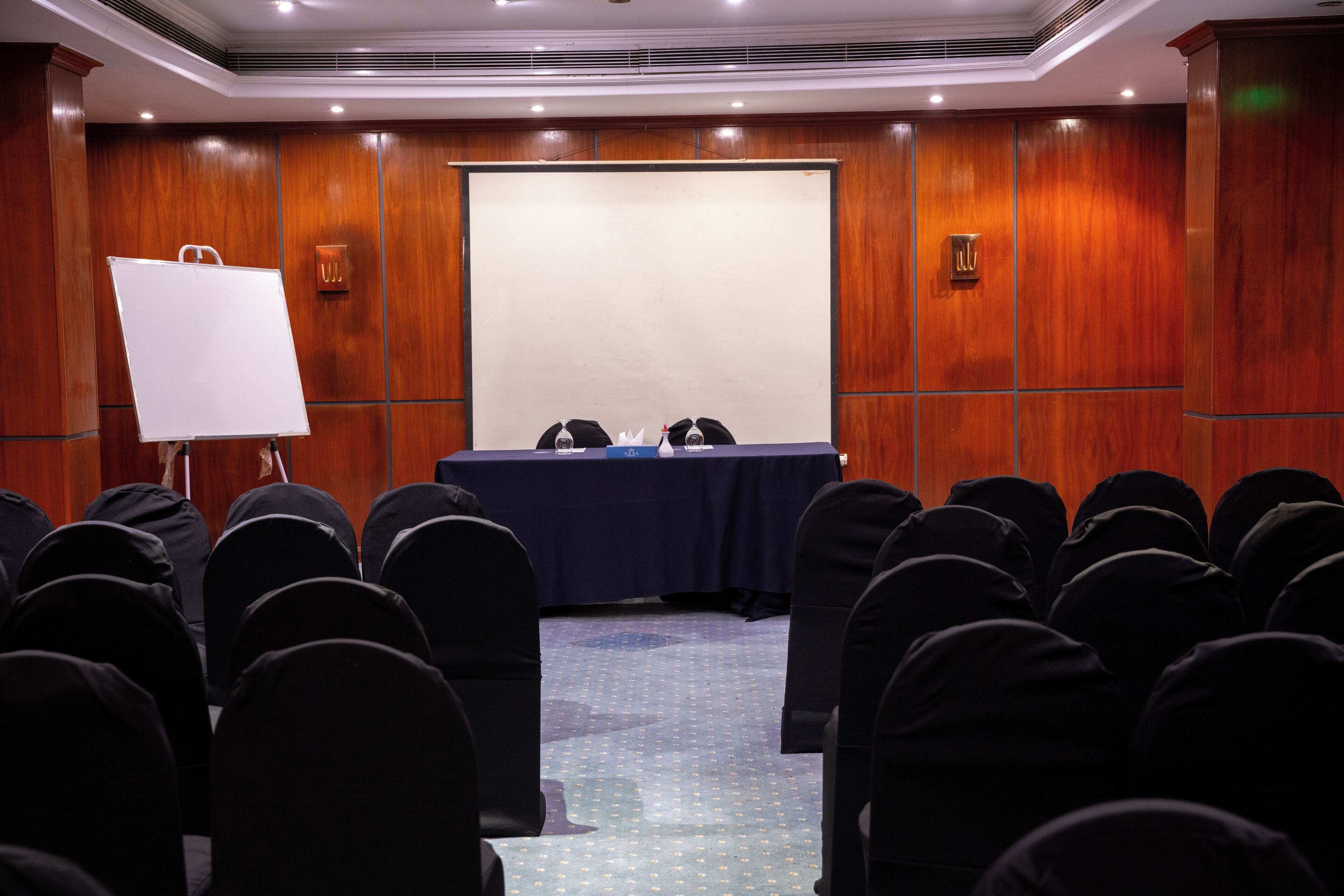 A conference room with a whiteboard, a table with nameplates, and rows of chairs.