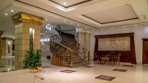 Un vestíbulo con piso de mármol, una escalera con barandillas ornamentadas y un mural grande en la pared.