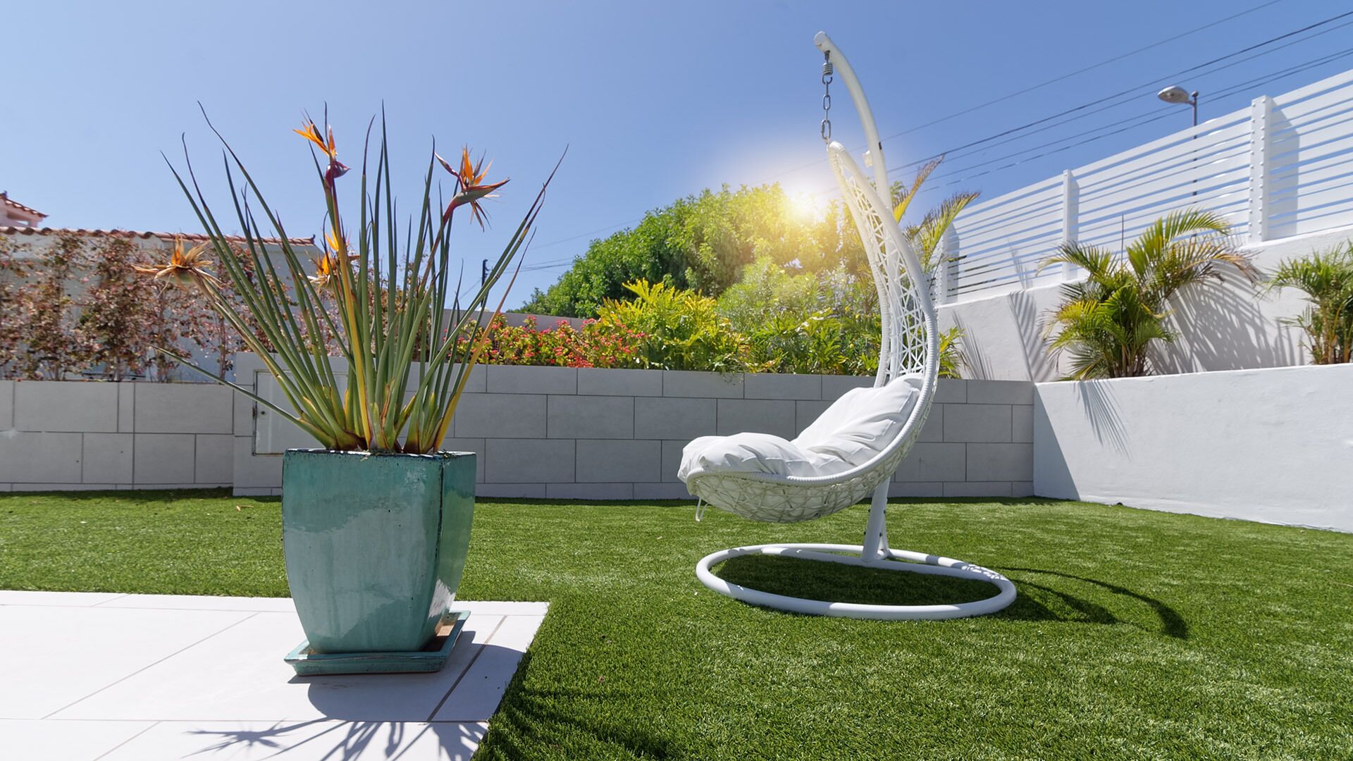 Un jardin avec du gazon synthétique, un fauteuil suspendu et une grande plante en pot.
