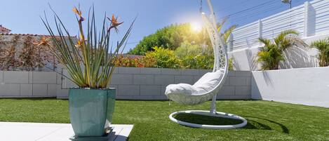 Un jardin avec du gazon synthétique, un fauteuil suspendu et une grande plante en pot.