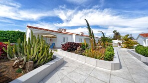 A white building with a red-tiled roof, surrounded by a landscaped garden with cacti and various plants. - Bungalows Adonis (San Bartolomé de Tirajana)