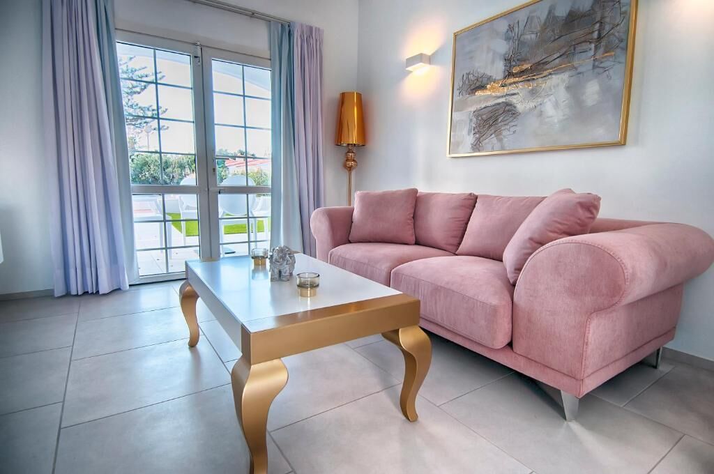 Ein rosafarbenes Sofa, ein Couchtisch mit Glastischplatte, eine Lampe und ein Bild an der Wand.
