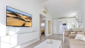 A modern living room with a large flat-screen TV, a white coffee table, and a beige sofa. - Bungalows Adonis (San Bartolomé de Tirajana)