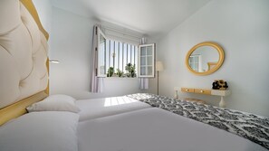 A hotel room with a large bed, a bedside table, a mirror, and a window with curtains. - Bungalows Adonis (San Bartolomé de Tirajana)