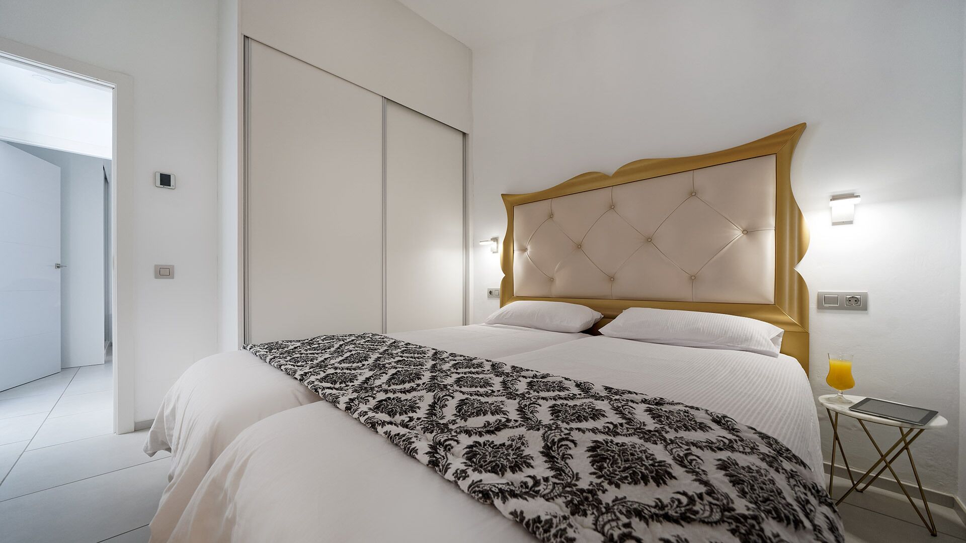 Habitación de hotel con una cama grande, una mesita de noche con un vaso de zumo de naranja y un diseño moderno.