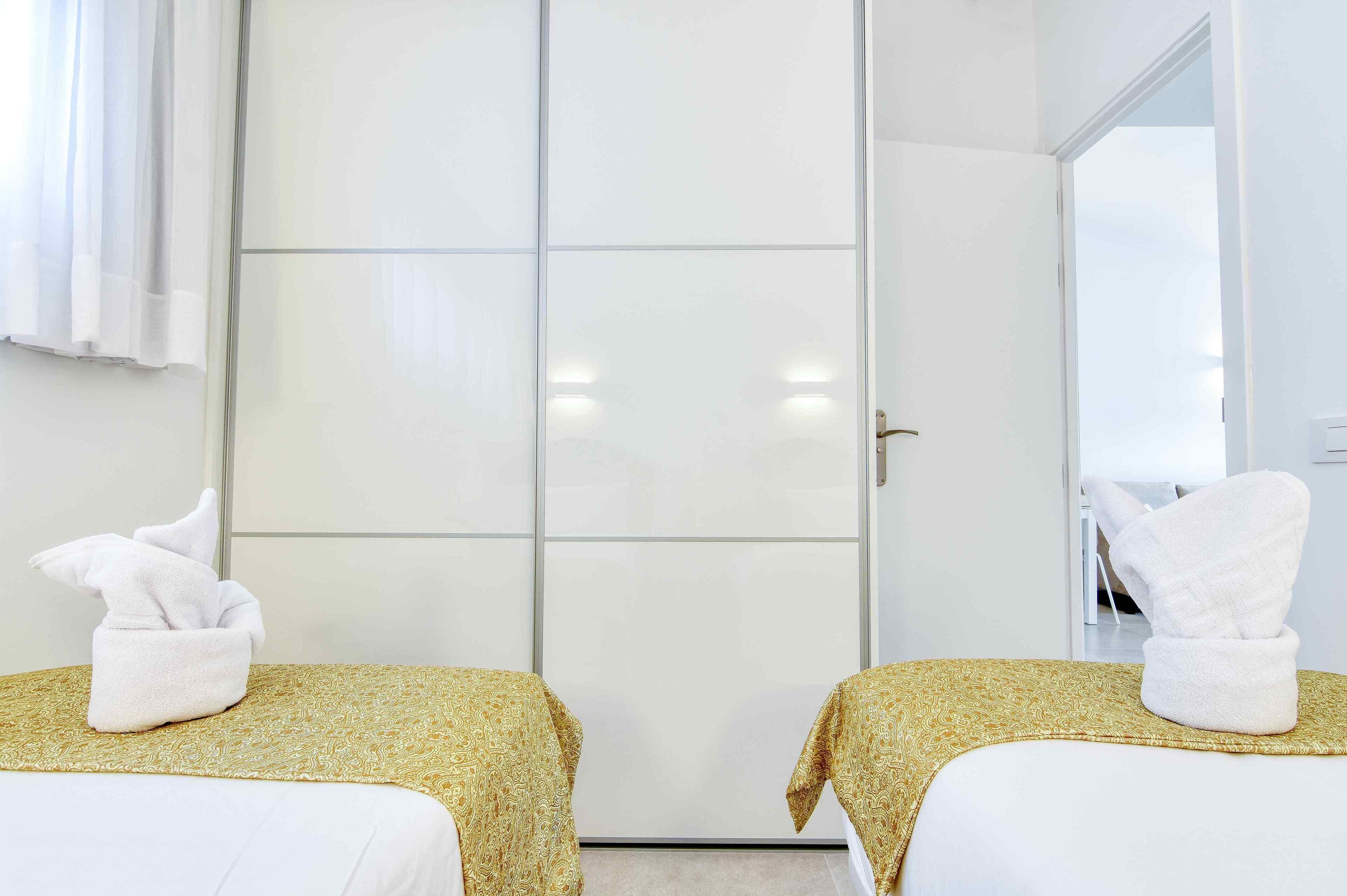 A hotel room with two beds, each with a golden patterned bedspread and a white towel folded on top.