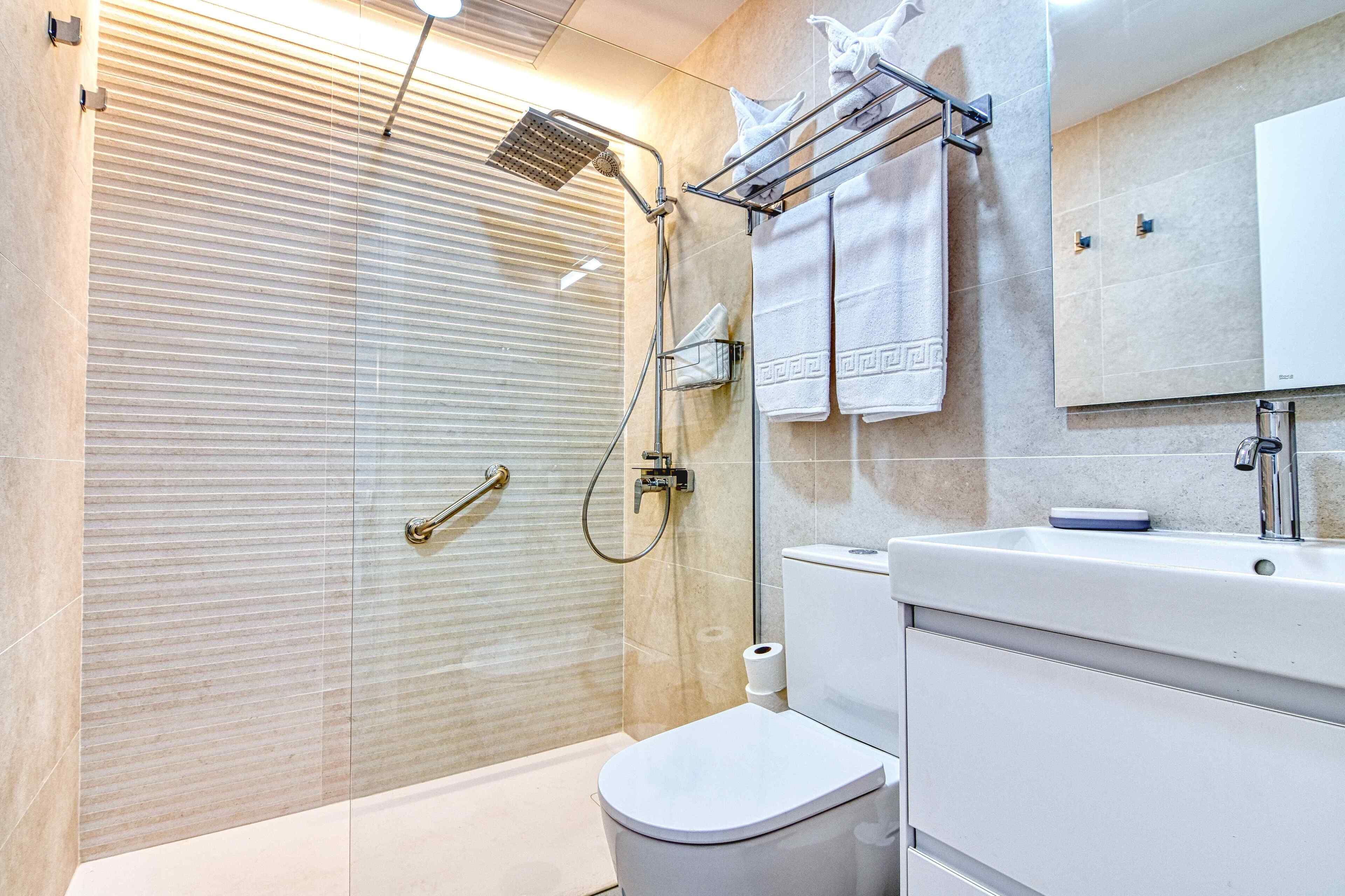 A modern bathroom with a glass shower enclosure, a toilet, a sink with a mirror, and a towel rack with multiple towels.