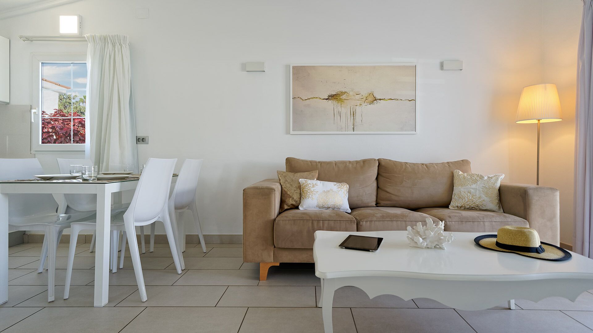Una sala de estar moderna con un sofá color beige, sillas blancas, una mesa de comedor y un cuadro en la pared.