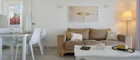 Una sala de estar moderna con un sofá color beige, sillas blancas, una mesa de comedor y un cuadro en la pared.