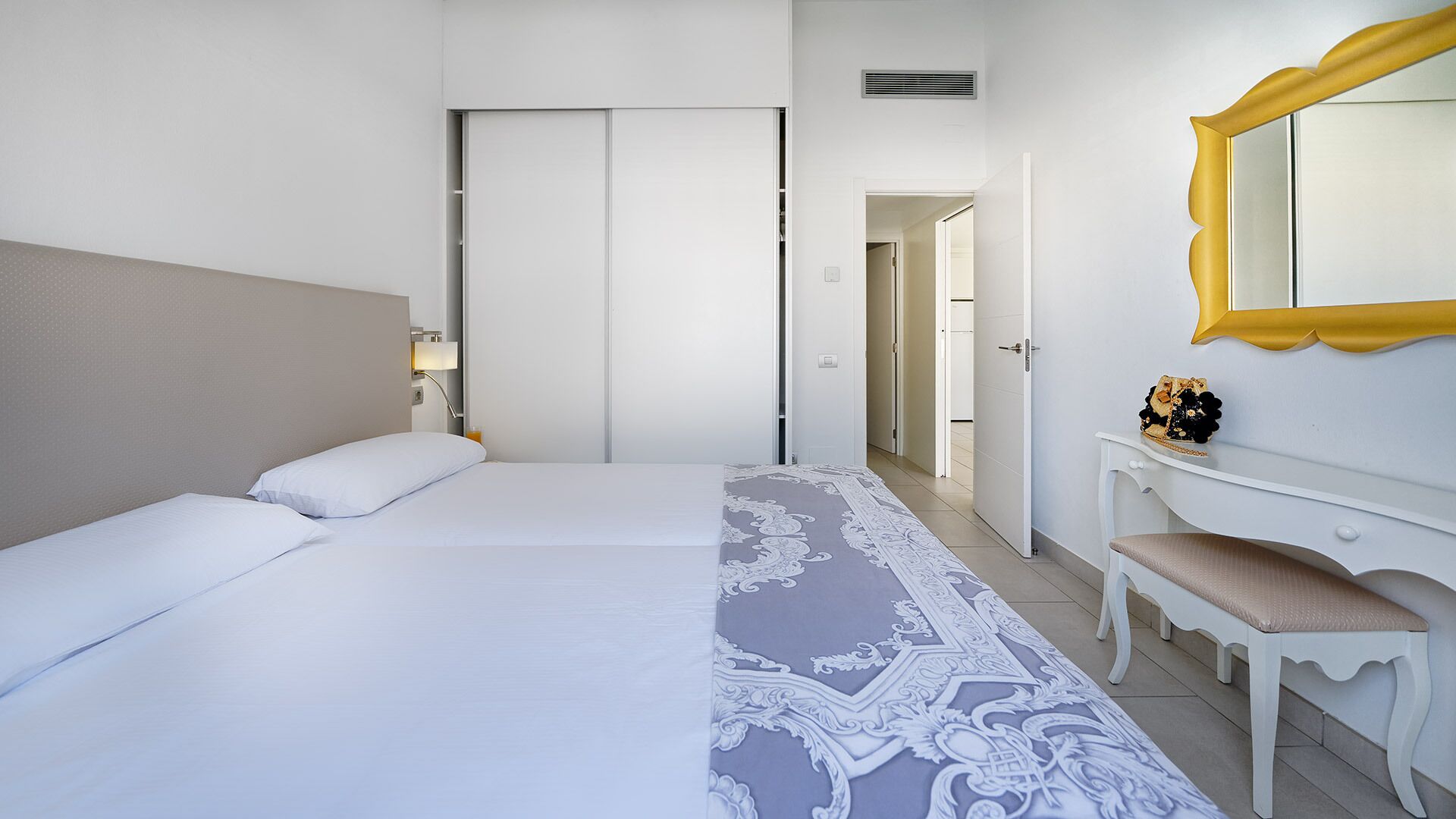 Una habitación de hotel con cama, escritorio, silla, espejo y puerta que da a otra habitación.