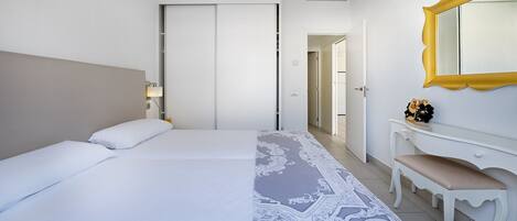 Una habitación de hotel con cama, escritorio, silla, espejo y puerta que da a otra habitación.
