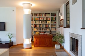 Ein Wohnzimmer mit Kamin, Bücherregal, Couchtisch aus Holz und einer großen Stehlampe.