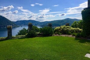 A well-maintained lawn, stone pillars, and a view of a lake and mountains.