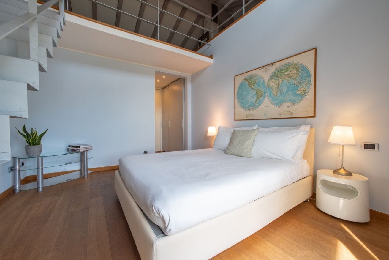 Camera da letto moderna con un letto grande, un tavolino in vetro con una pianta, una mappa appesa al muro e una scala.