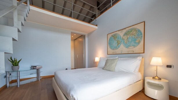 A modern bedroom with a large bed, a glass table with a plant, a map on the wall, and a staircase.