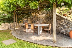 A stone patio with a wooden pergola, a table, and chairs.