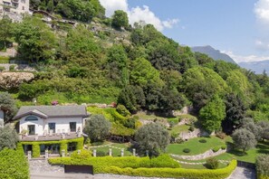 A hillside villa with a well-manicured garden, a stone pathway, and a view of the surrounding forest.