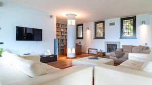A modern living room with a flat-screen TV, a fireplace, a bookshelf, and a large pillar light.