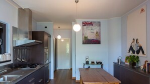 A modern kitchen with stainless steel appliances, a wooden dining table, and a wall-mounted painting of a British cityscape.
