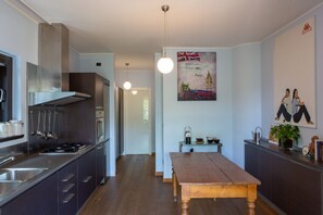 Une cuisine moderne équipée d’appareils électroménagers en acier inoxydable, une table à manger en bois et un tableau représentant un paysage urbain britannique, accroché au mur.