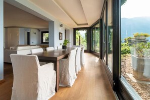 A modern dining area with a long table, white chairs, and a view of a mountainous landscape through large windows.
