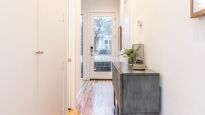 A hallway with a wooden floor, a dark console table with a plant, and a door leading to a glass door with a view of a house. - Stylish & Perfectly Located Deluxe 2-Bed Townhome (Dallas)