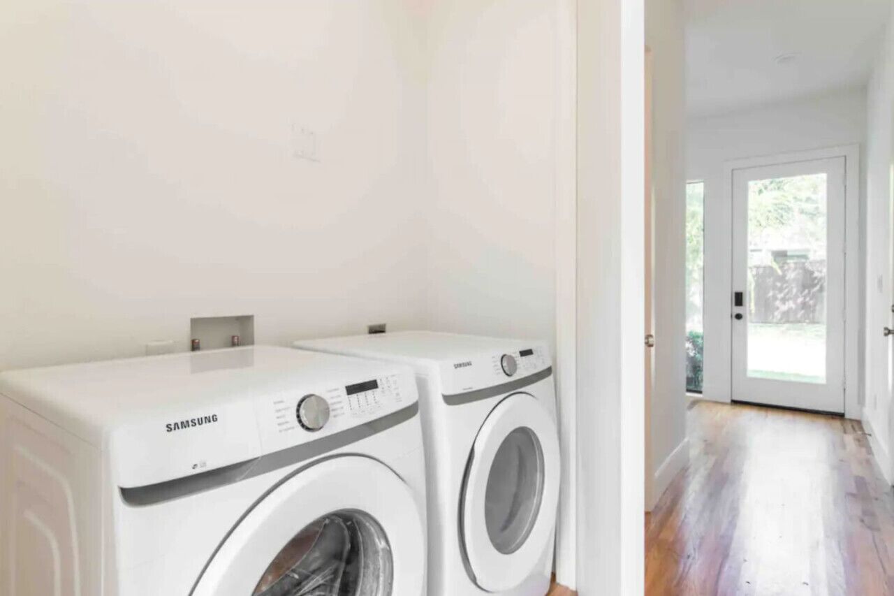 A laundry room with two Samsung washing machines and a wooden floor.