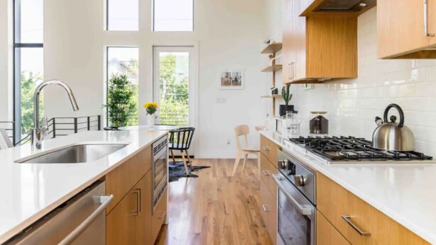 A modern kitchen with a central island, stainless steel appliances, and a view of the outdoors through large windows. - Glamorous Perfectly Located Deluxe 2 Bed Townhome (Dallas)