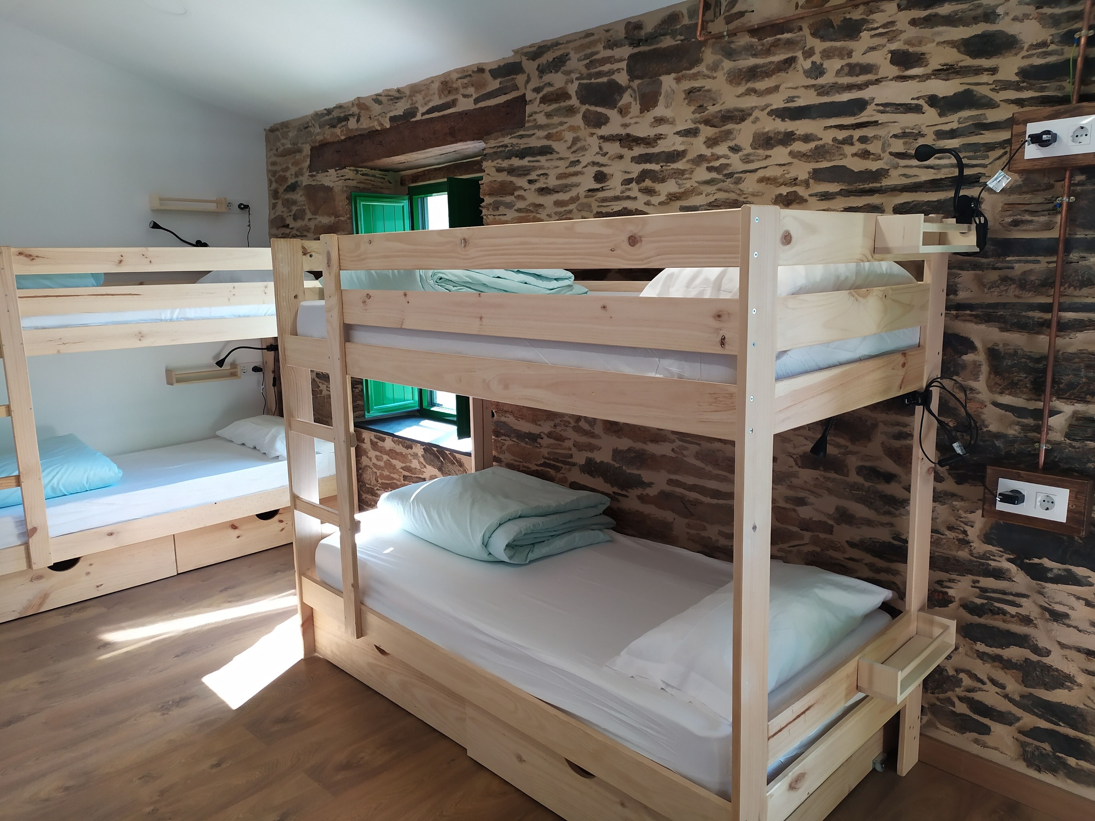Ein Schlafraum mit Etagenbetten, einer Steinwand und Holzdielen.