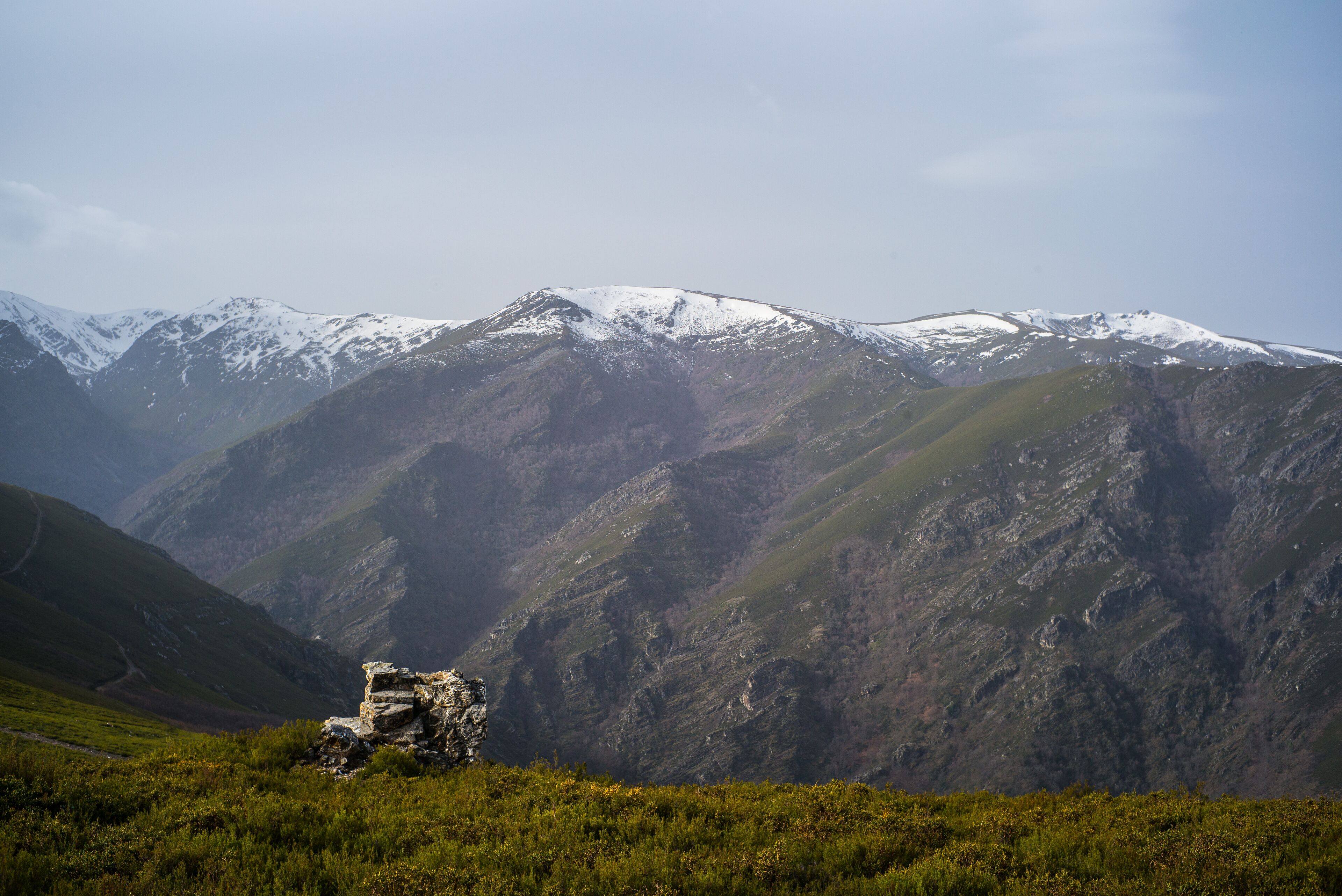 Un paisaje montañoso con un afloramiento rocoso en primer plano y picos nevados al fondo.