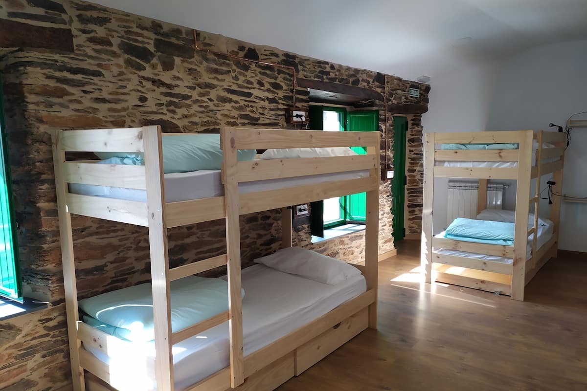 Une pièce avec des lits superposés adossés à un mur en pierre, une porte verte et un plancher en bois.