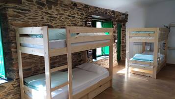 A room with bunk beds against a stone wall, a green door, and a wooden floor.