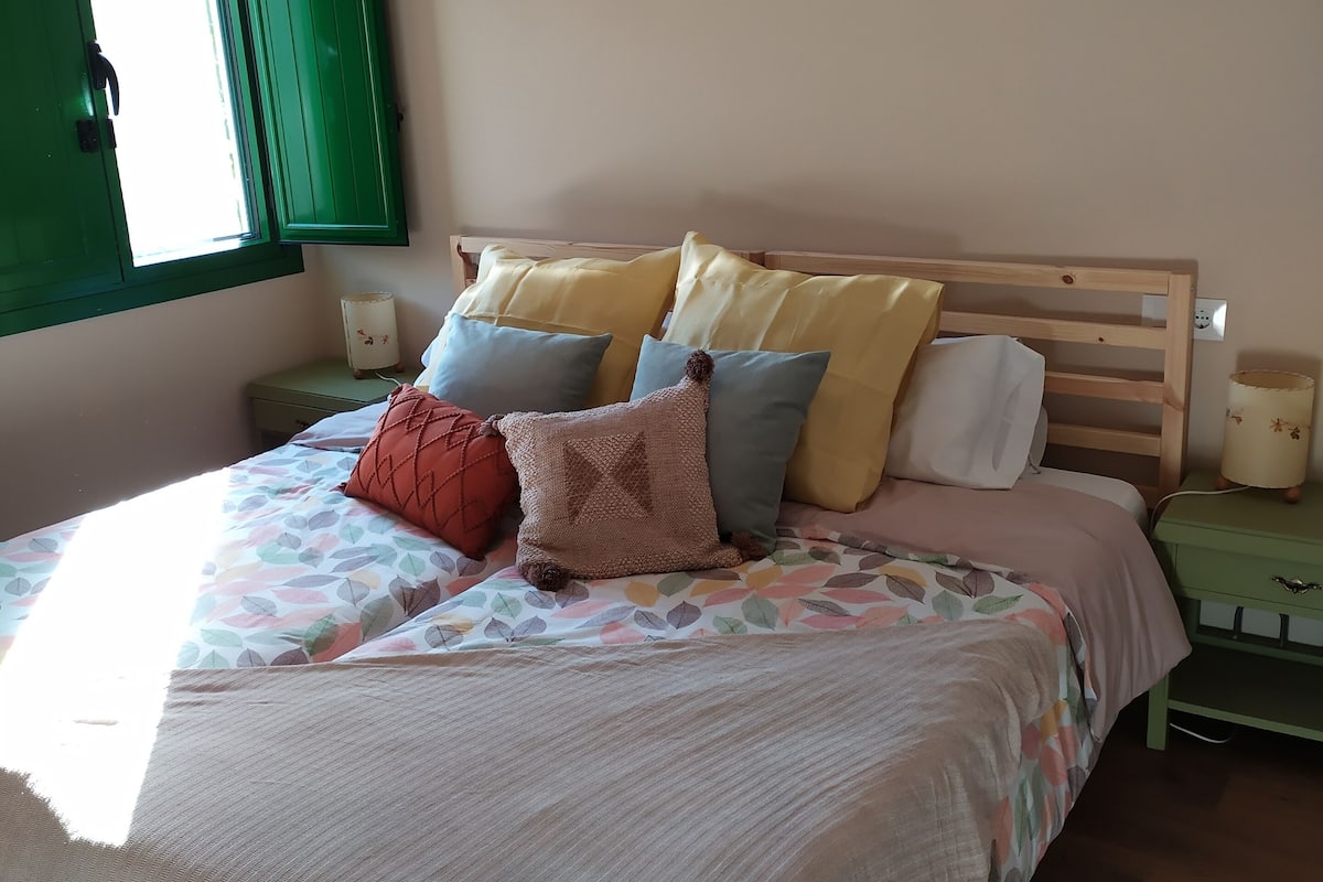 Un lit avec une couvre-lit à motifs floraux, plusieurs oreillers et une tête de lit en bois.