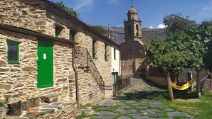 A stone building with a green door, a staircase, and a bell tower in the background. - Eco dos Teixos (Carballeda de Valdeorras)