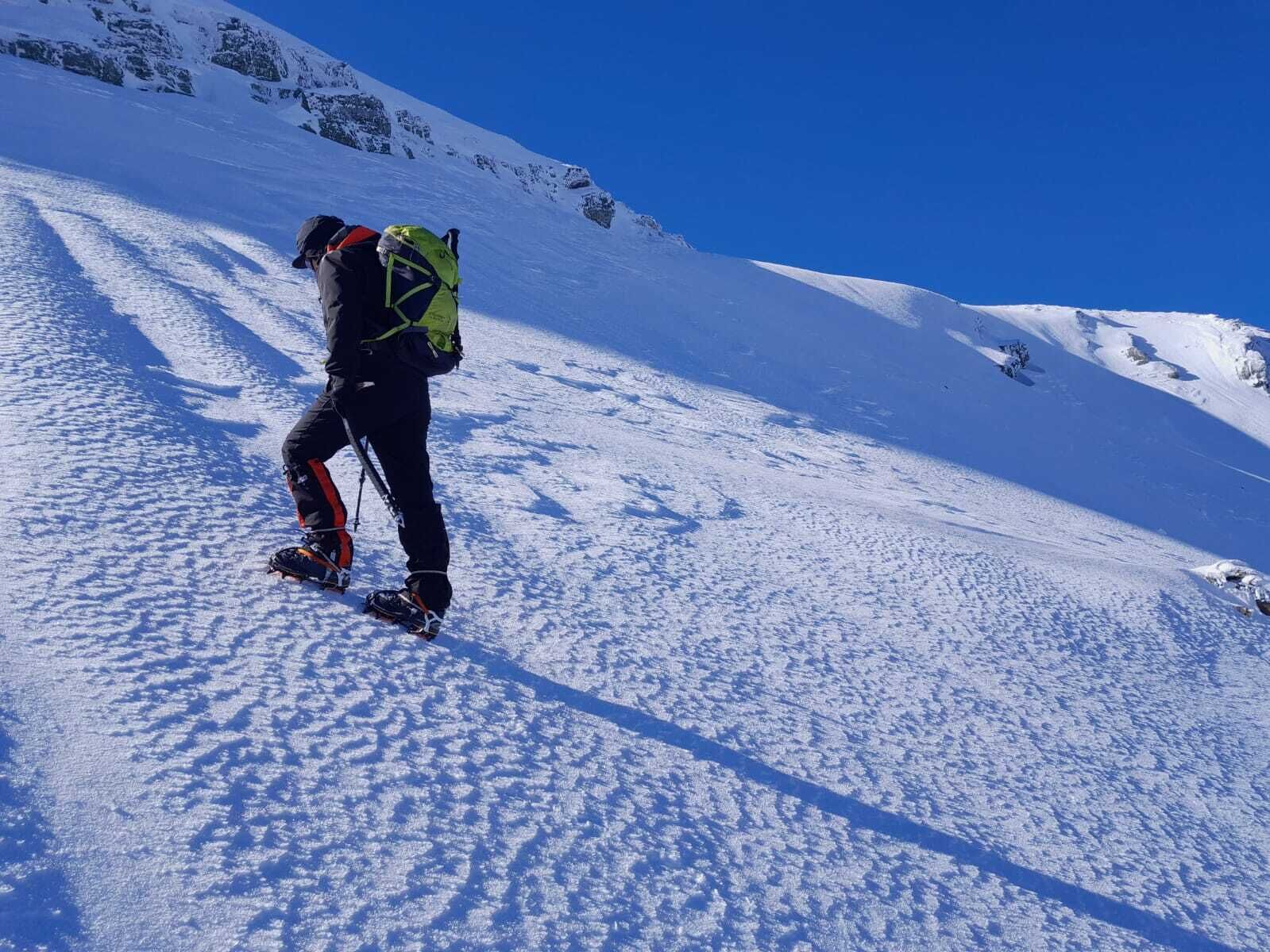 En person som klättrar uppför en snötäckt bergssluttning med en ryggsäck.